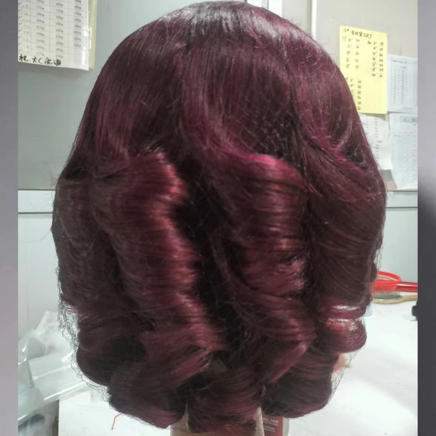 Burgundy wig with wavy hair style on a plain background