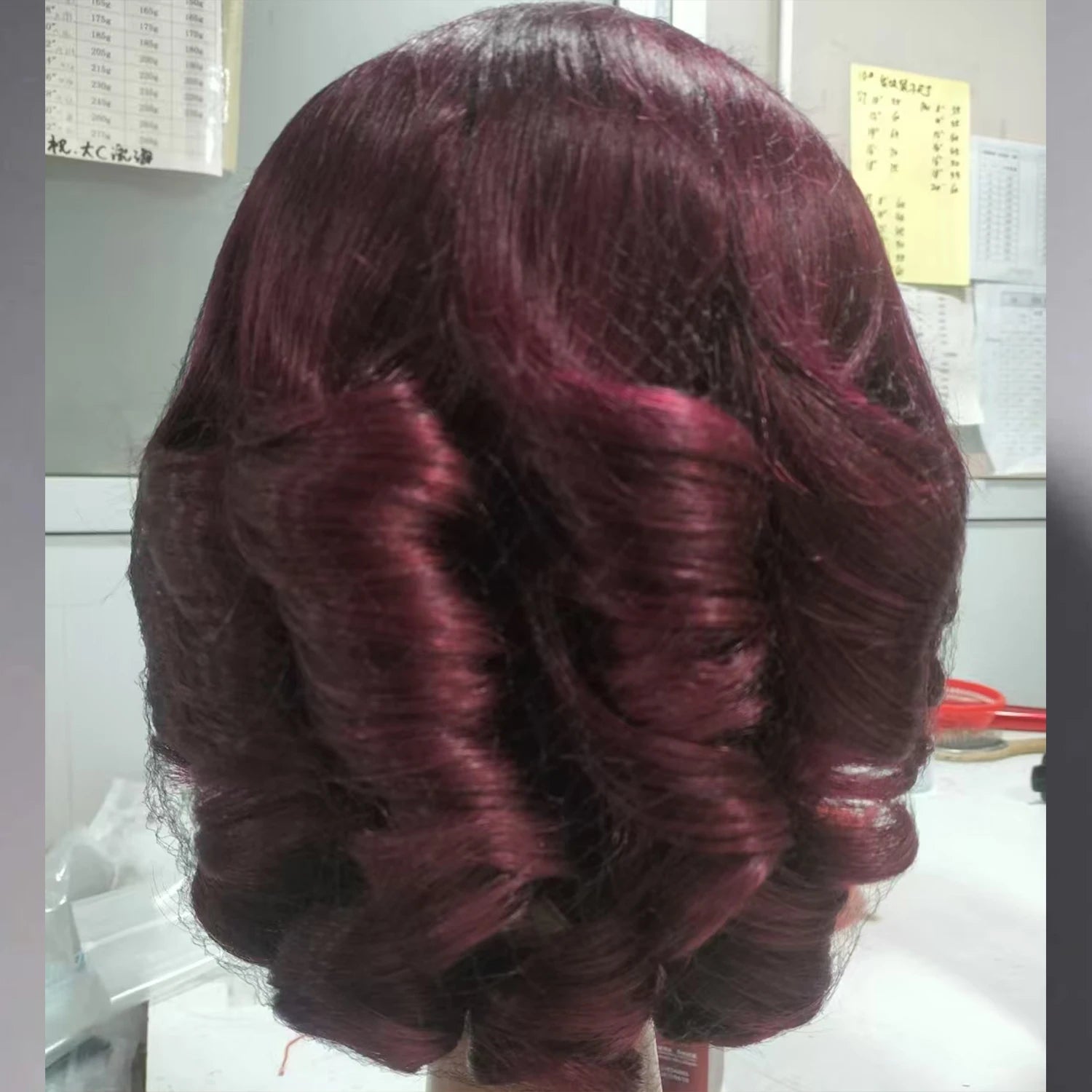 Burgundy wig with wavy hair style on a plain background