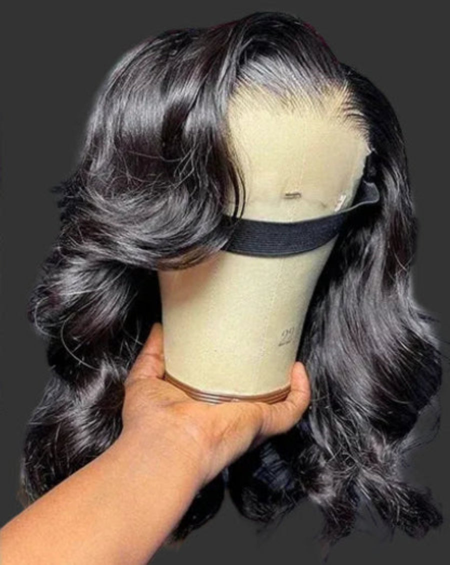 Black wavy hair wig on a mannequin head with a visible brand logo in the background.